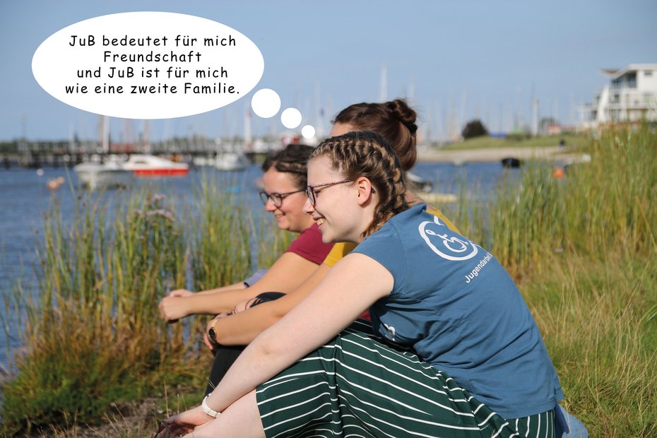 Junge Frau sitzt neben zwei anderen und schaut auf einen See: "JuB bedeutet für mich Freundschaft und JuB ist für mich wie eine zweite Familie."