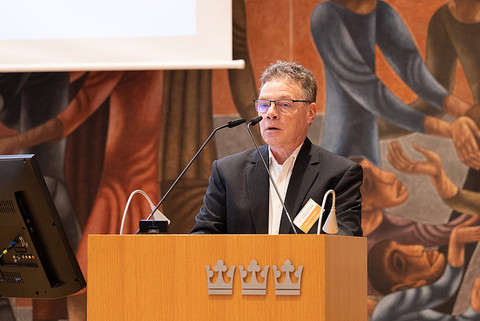 Pfarrer Ziegler am Mikrofon. Man sieht ihn hinter dem Pult und Mikrofon. Das Pult ist mit drei Kronen verziert.