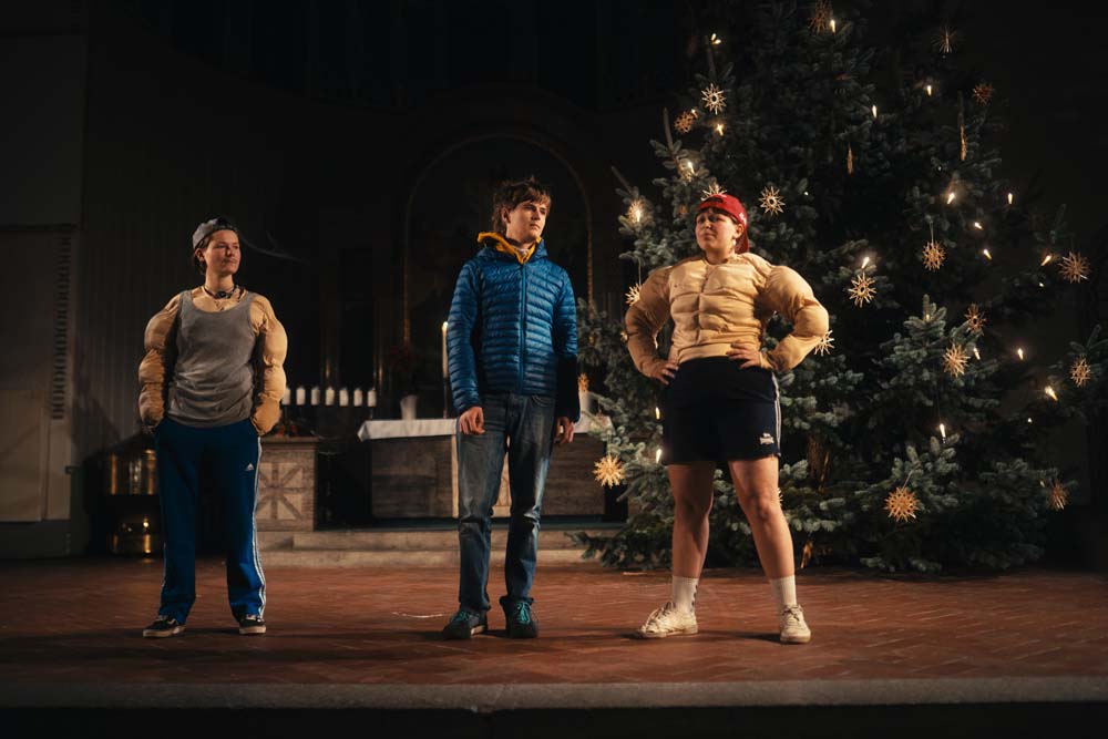 Drei Personen im Gespräch. Davon tragen zwei Muskelshirts und sehen aus als würden sie ihre Muskeln trainieren.