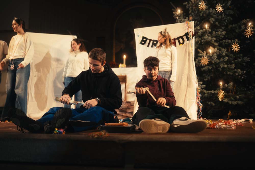 Im Fordergrund sitzen zwei Junge Hirten, die Schnitzen. Im Hintgrund hängen Bettlaken und ein Spruchband mit "Birthday".