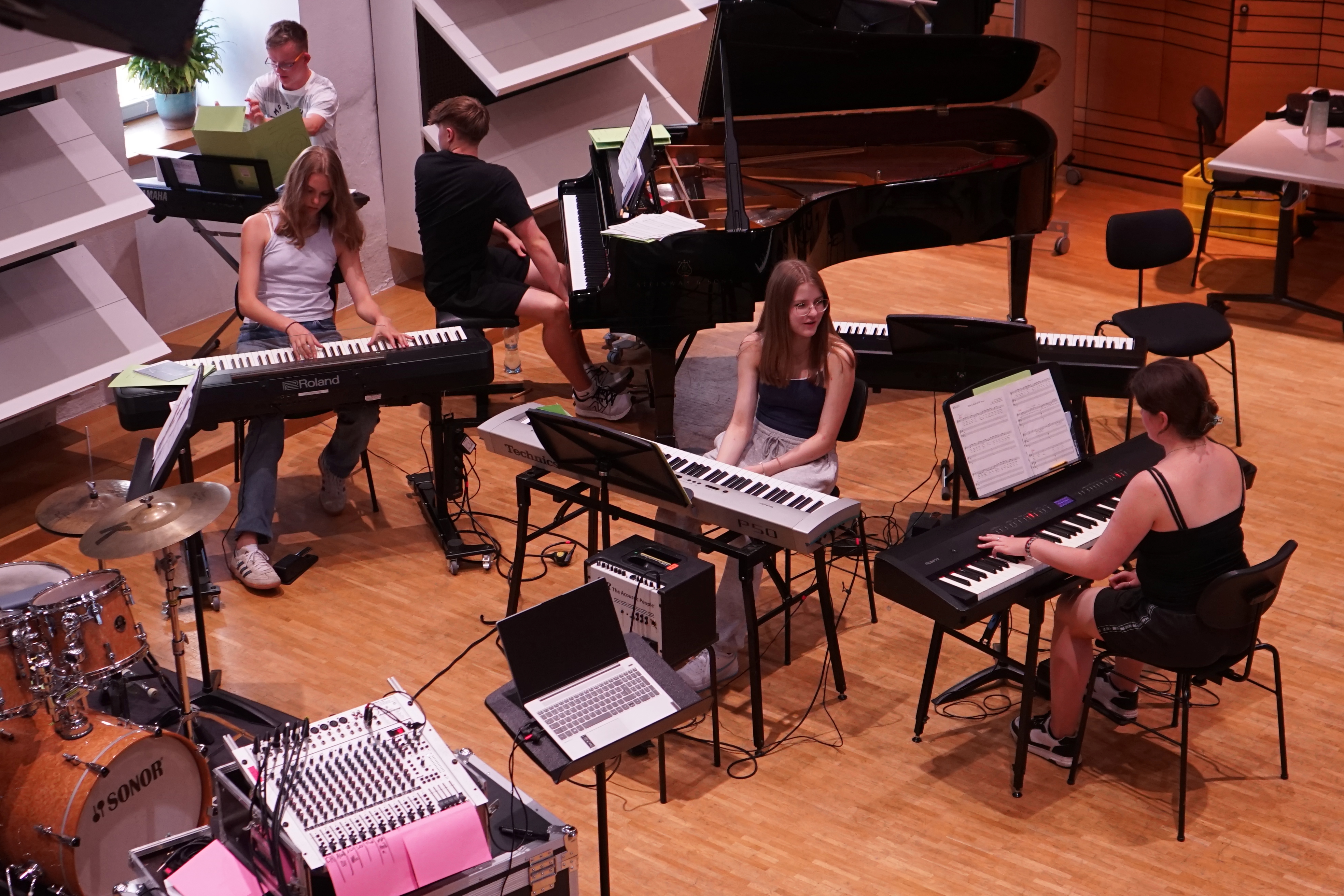 Vier E-Pianos stehen da. Jugendliche sitzen davor. Man sieht auch ein Schlagzeug.