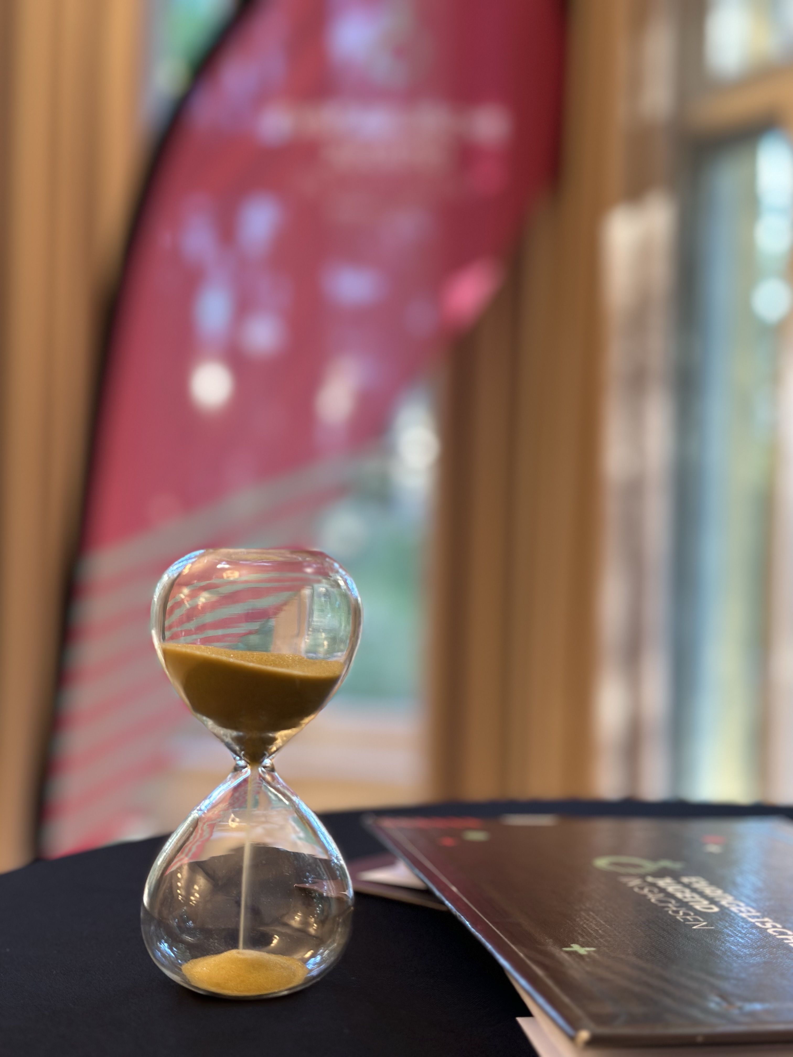 Eine Sanduhr steht auf einem Tisch, daneben ein Klemmbrett der Evangelischen Jugend